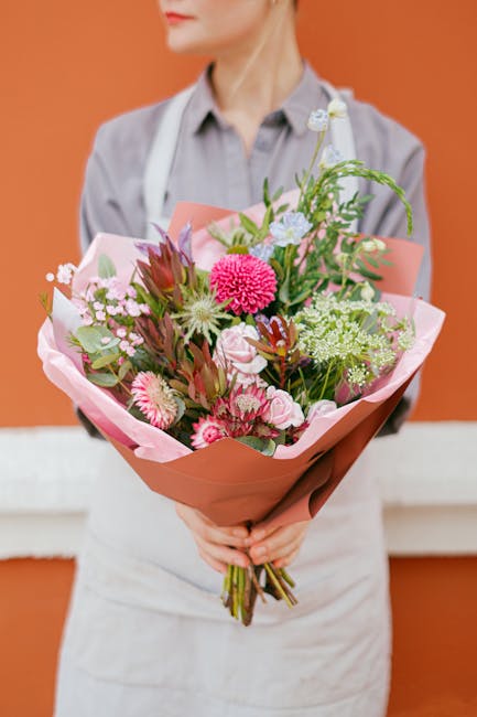 A floral bouquet featuring a vibrant mix of fresh pink, white, and green flowers, including chrysanthemums, roses, and filler foliage, arranged in a lush, full style. The bouquet is wrapped in light p
